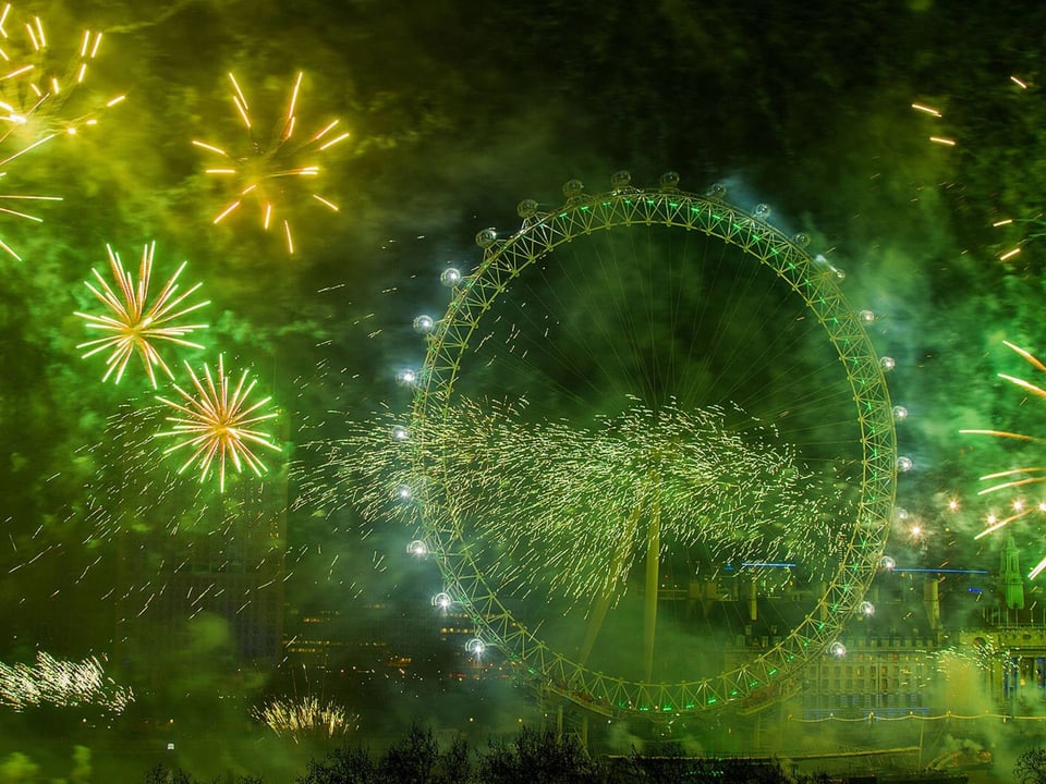 Das Riesenrad im grünen Licht von explodierendem Feuerwerk.