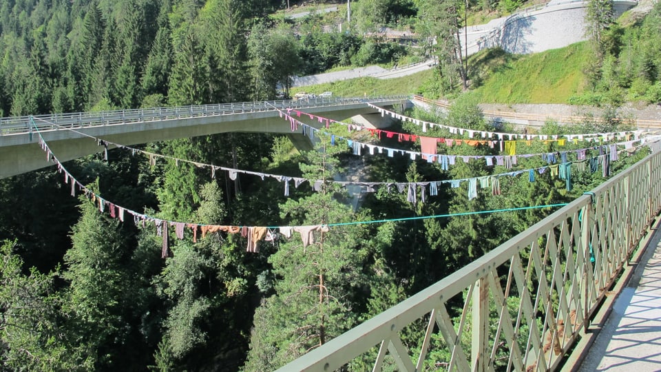 Bunte Kleidungsstücke sind auf eine Wäscheleine zwischen zwei Brücken gespannt.