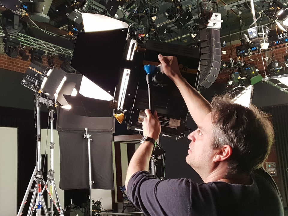 Der Chef-Kameramann Matthias Bolliger hantiert an einem grossen Studio-Scheinwerfer herum.