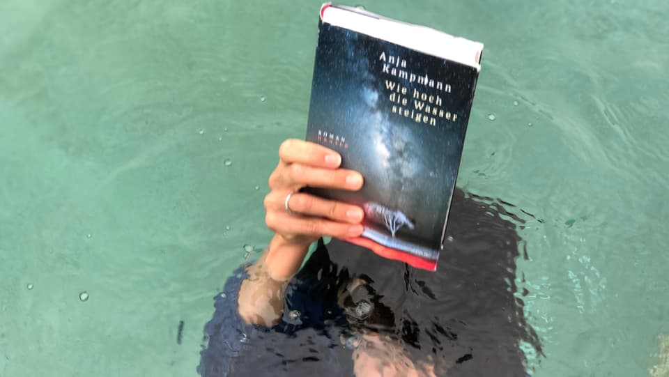 Annette König ist unter Wasser und hält das Buch von Anja Kampmann «Wie hoch die Wasser steigen» über das Wasser