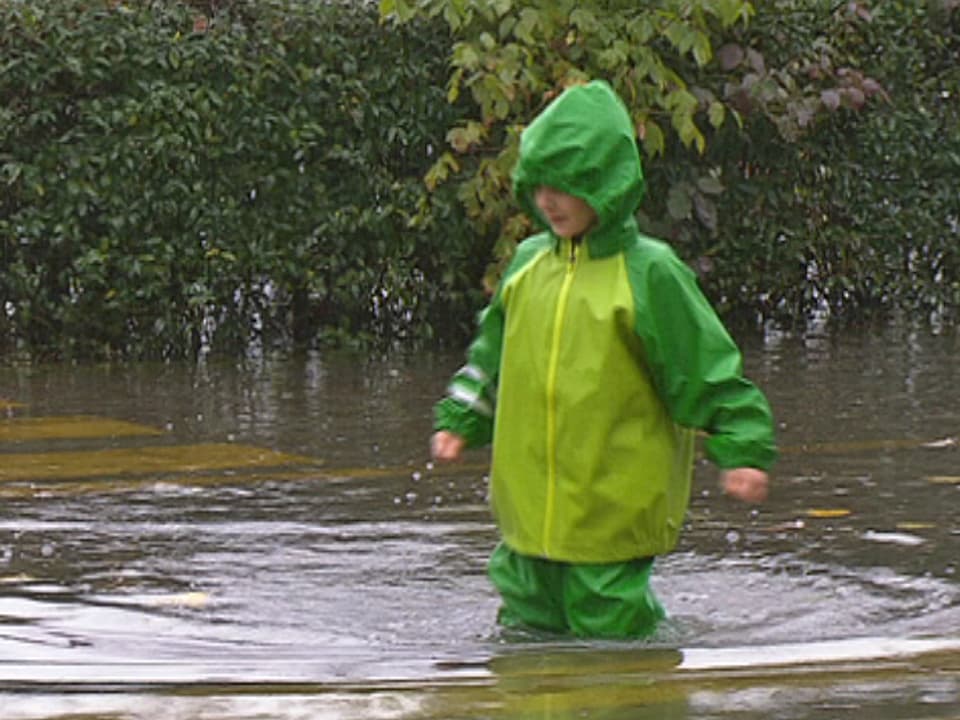 Ein Kind im Regenzeug stapft durch knietiefes Wasser.