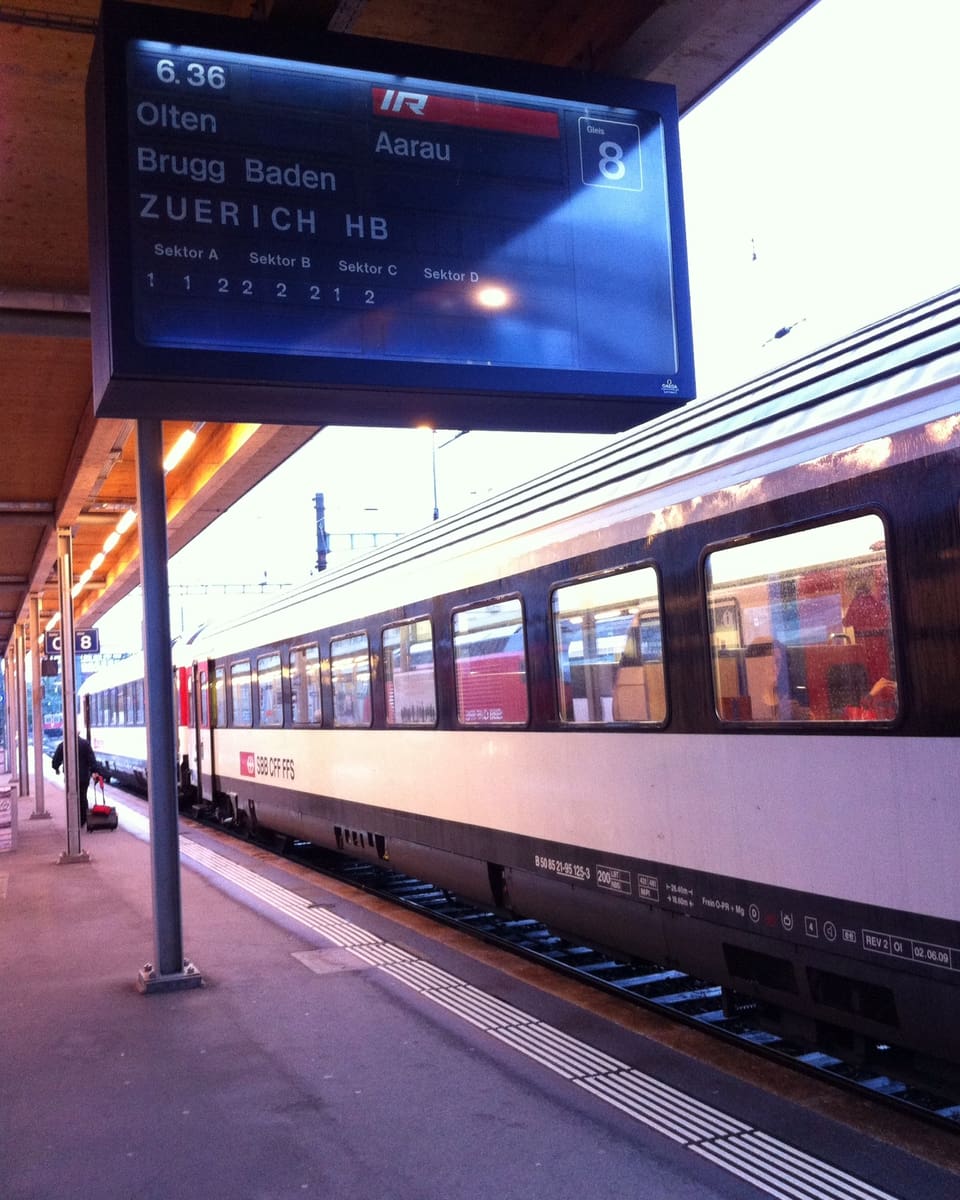 Ein Zug fährt am Bahnhof ein. Auf einer Tafel wird angezeigt, dass der Zug um 6 Uhr 36 Minuten nach Aarau fährt.