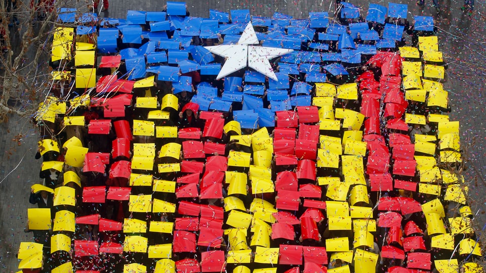Mit roten, gelben, blauben und weissen Plakaten formen Katalanen ihre Regionalflagge auf einer Strasse (Aufnahme von oben).