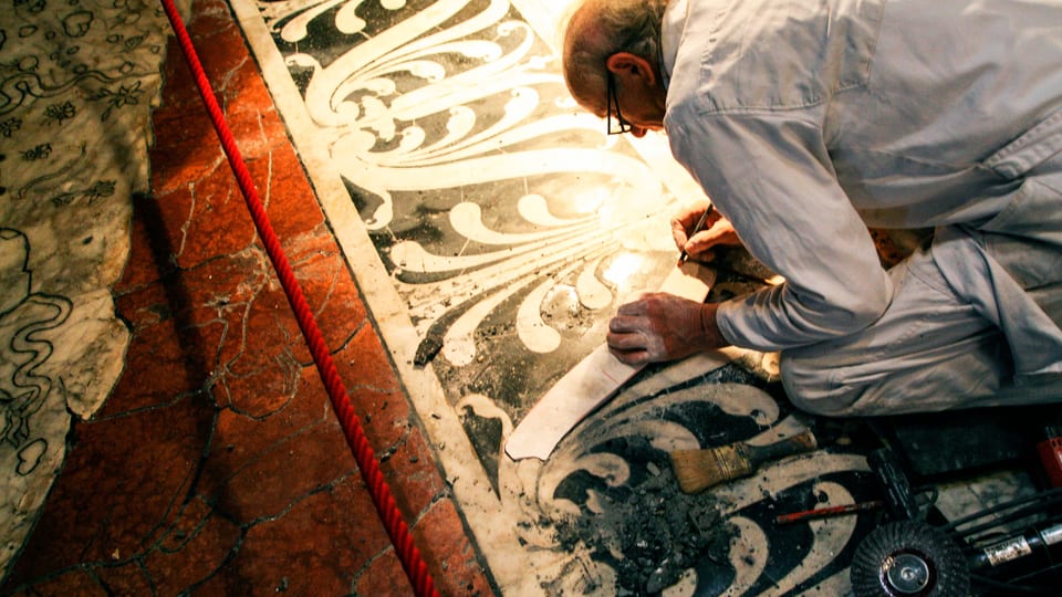 Ein Mann kniet auf dem Boden und restauriert die Marmorplatten.
