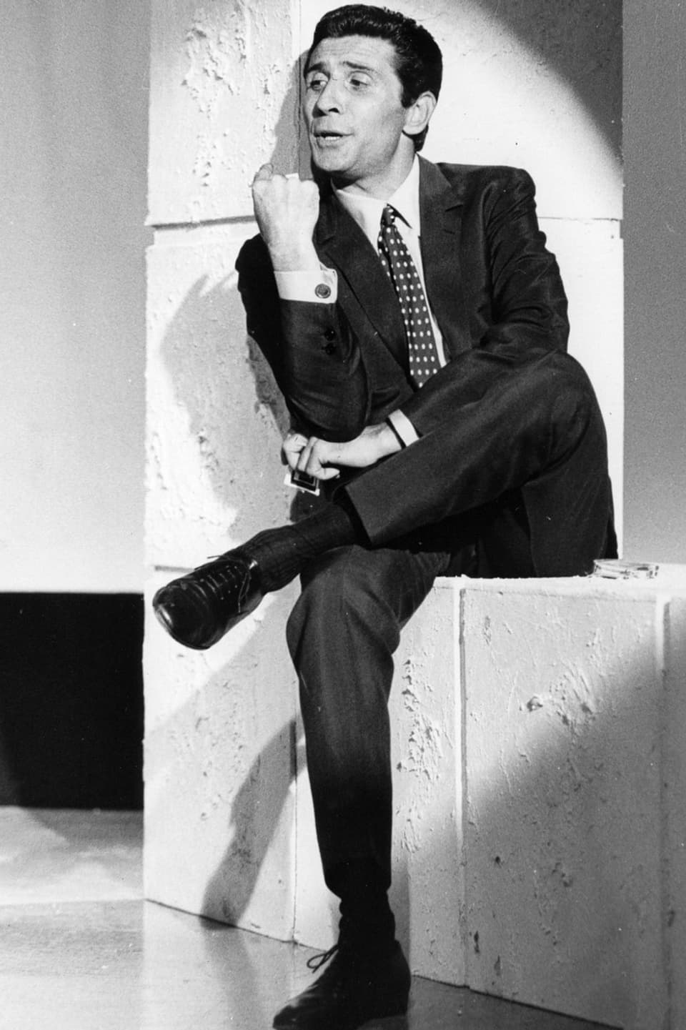 Ein Mann im dunklen Anzug sitzt auf einer weissen Mauer.