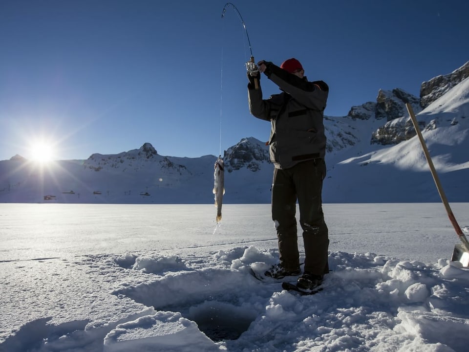 Ein Mann steht auf dem gefrorenen Melchsee. Er hat einen Fisch an seiner Angel.