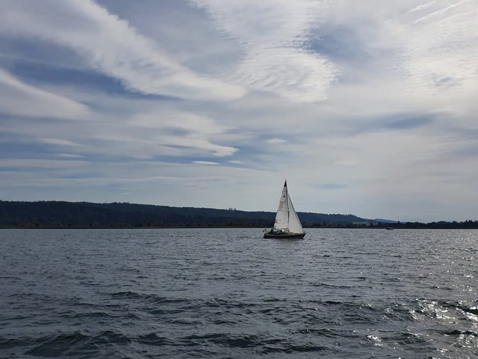 Segelschiff auf einem See unter leicht bewölktem Himmel