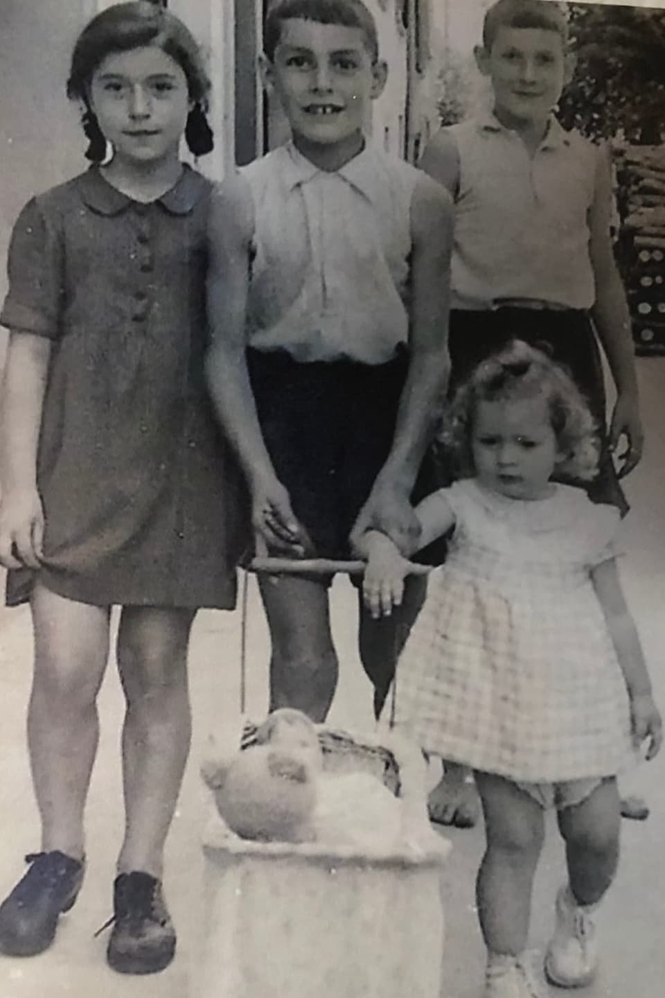 Vier Kinder mit einem Puppenwagen.