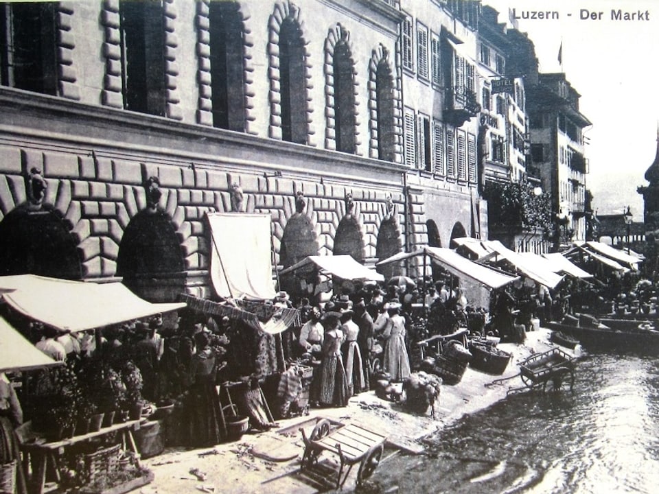 Historisches Bild von einem Markt an einem Fluss mit vielen Ständen und vielen Leuten. 