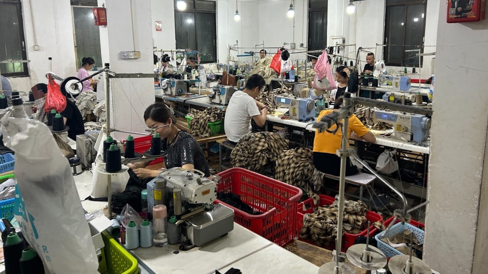 Zahlreiche Näherinnen und Näher sitzen in einer Werkstatt an ihren Nähmaschinen.