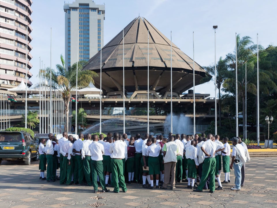 Eine Gruppe junger Leute in weiss-grüner Uniform steht vor einem Gebäude, das wie ein umgedrehter Diamant aussieht. 