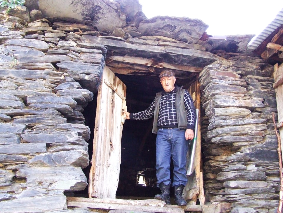 Ein Mann steht vor einer halb geöffneten, hölzerner Tür eines steinernen Hauses.