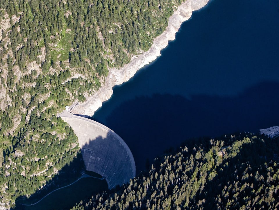 Luftaufnahme der Staumauer des Lago del Sambuco im Tessin. An den Hängen um den See hat es Bäume.