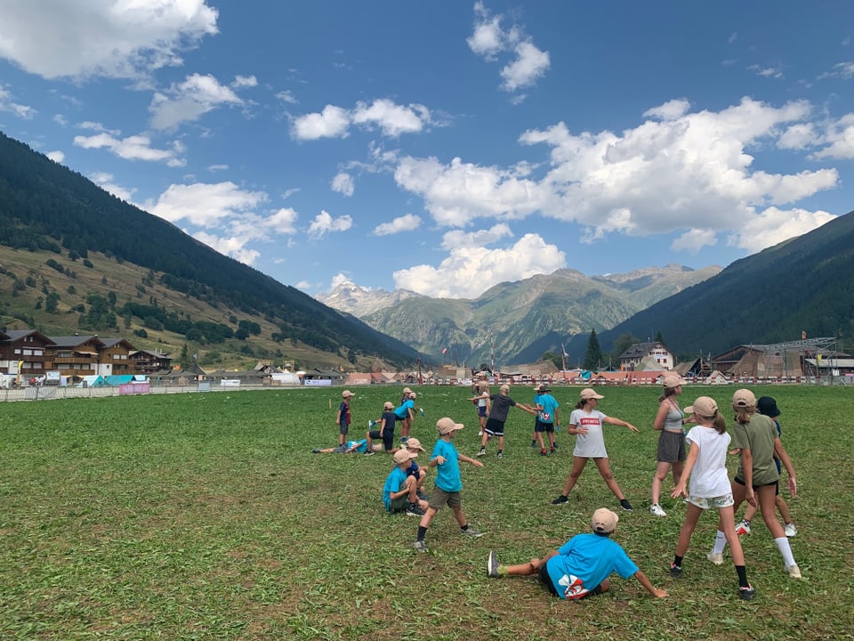 Kinder spielen auf einer Wiese und im Hintergrund eine Berglandschaft