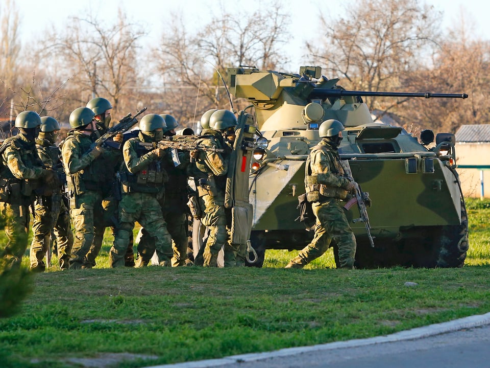 Schwerbewaffnete Soldaten neben Panzerfahrzeug.