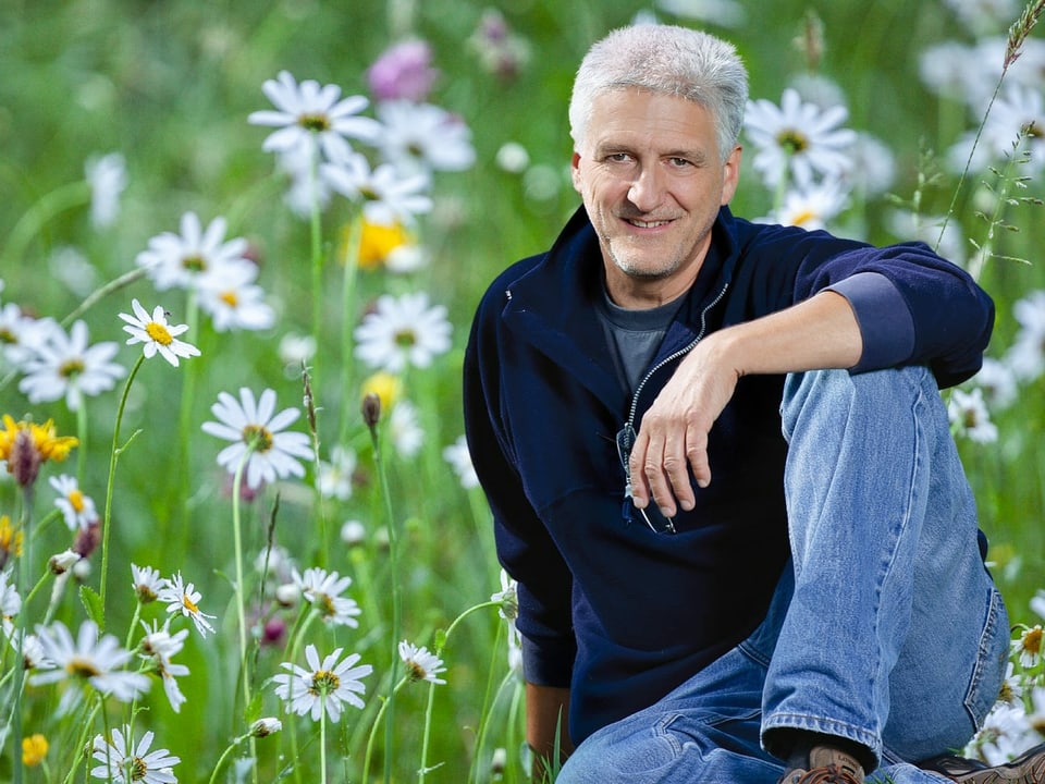 Andreas Moser sitzt in einer Blumenwiese.