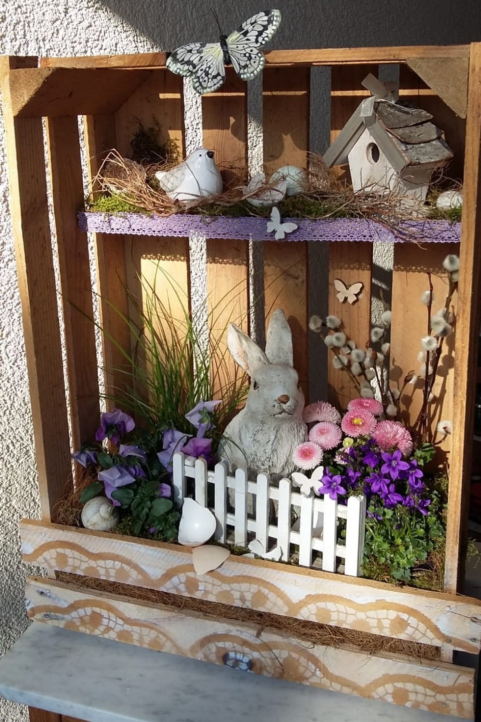 Bunt dekorierte Holzkiste mit Hasen Blumen Vogelhäuschen. 
