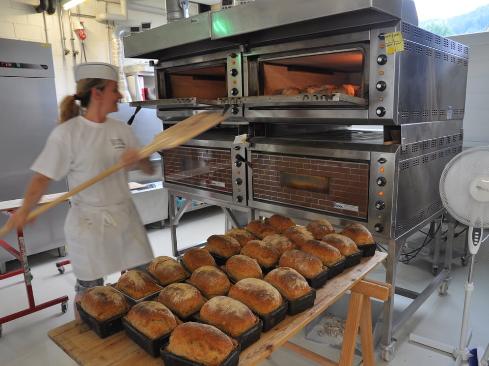 Eine Bäckerin nimmt mit einer Holzkelle Brote aus dem Backofen.