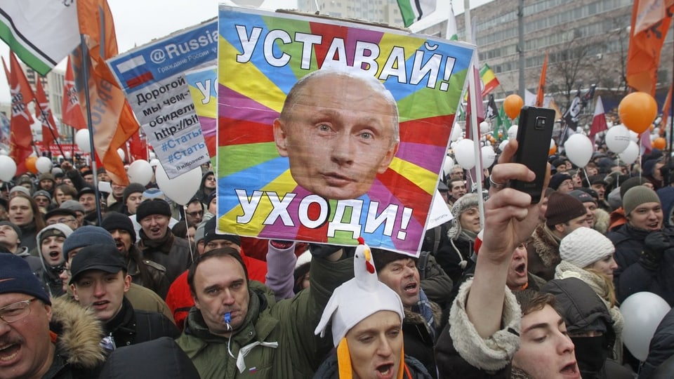 Ein farbiges Banner mit der Aufschrift «Werde müde! Geh weg!» (auf Russisch). Viele demonstrierende Menschen.