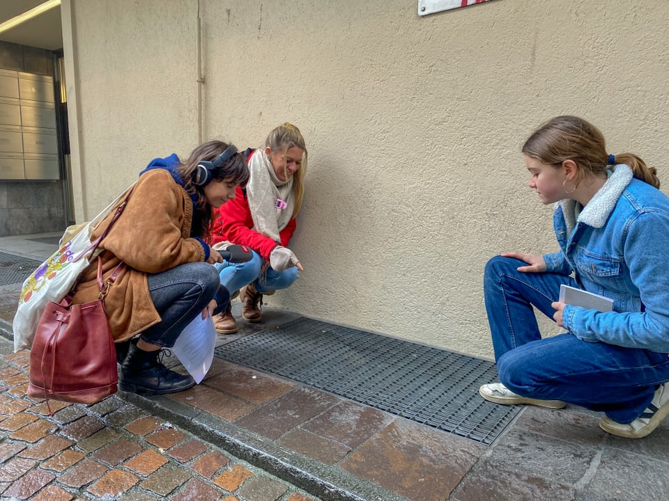 Ein Mädchen und zwei Frauen stehen bei einem Gitter in einer Gasse in Zürich und schauen hinein.