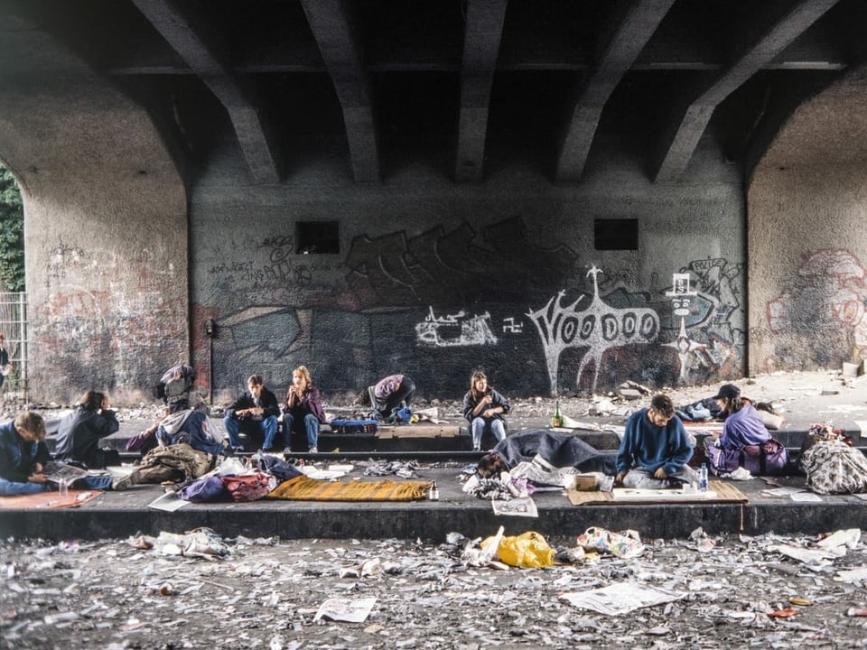 Menschen sitzen in einer dreckigen Umgebung auf alten Gleisen.