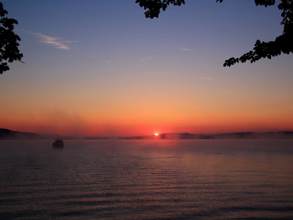 Die Sonne geht über dem See auf und verfärbt den Horizont rötlich.