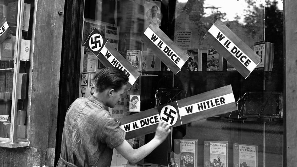 Ein junger Mann klebt Plakate auf das Fenster einer Buchhandlung in Rom, um das Treffen zwischen Mussolini und Hitler in München zu feiern.