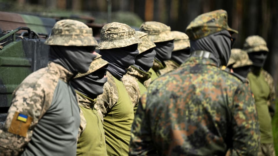 Gruppe von ukrainischen Soldaten in Tarnuniform mit Gesichtsbedeckungen stehen in einer Reihe.