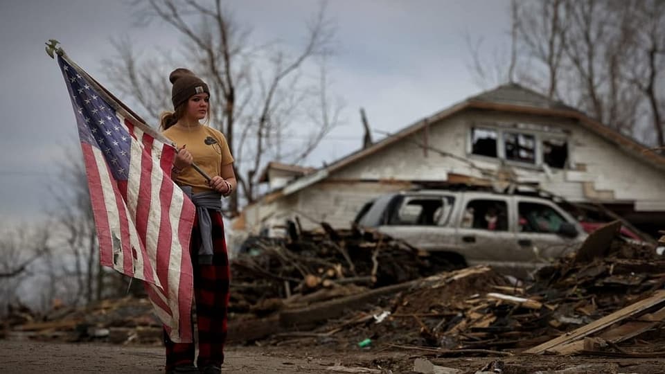 Teenagerin mit der US-Flagge vor Trümmern