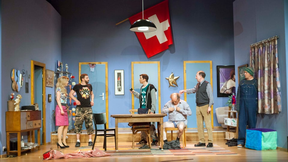 Sechs Schauspieler auf einer Theaterbühne, über ihnen thront die Schweizer Flagge.