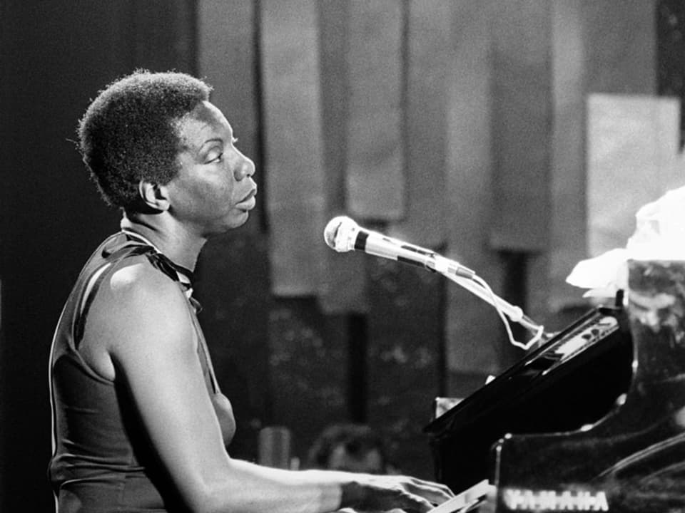 Frau mit kurzen Haaren (Nina Simone) sitzt am Piano und singt