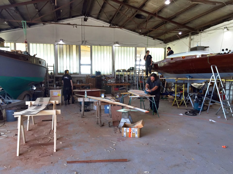 Werft-Halle. Darin stehen zwei Boote. Männer arbeiten mit Holz.