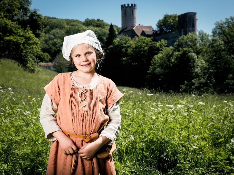 Junges Mädchen in mittelalterlicher Kleidung auf einer Wiese mit einer Burg im Hintergrund