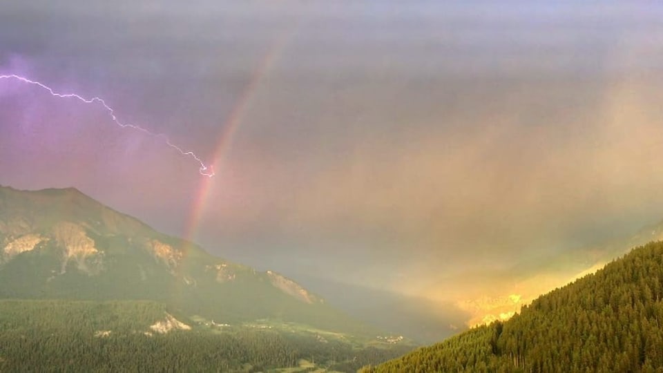 Mutten/GR Der Blitz hängt sich beim Regenbogen ein und die Sonne sendet dazu eine goldene Beleuchtung.
