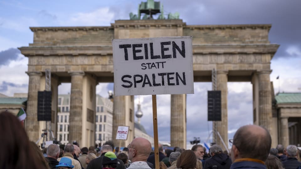 Brandenburger Tor im Hintergrund mit den hellen Säulen, davor Menschenmenge mit Schild «Teilen statt spalten»
