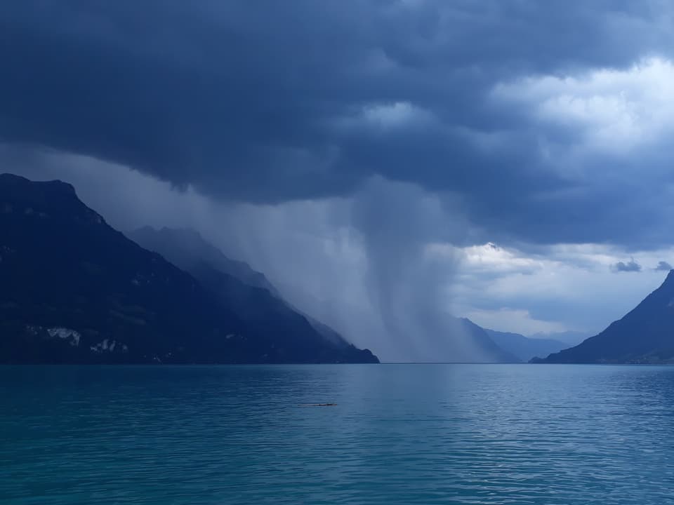 See mit Bergen und Regenschauer, der wie Fäden aus der Wolke hängt. 