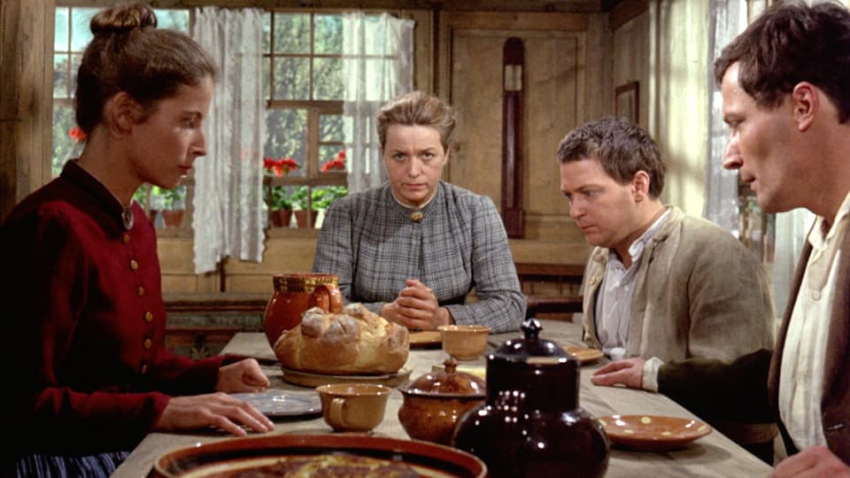 Szene am Abendtisch. Zwei Frauen und zwei Männer sitzen am Tisch und sprechen ein Tischgebet.