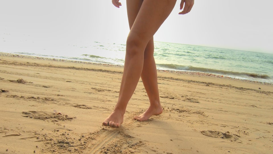 Am Strand malt eine Frau mit ihren Füssen Spuren in den Sand.