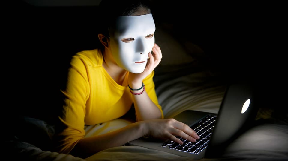Eine Frau mit weisser Maske sitzt vor dem Laptop.