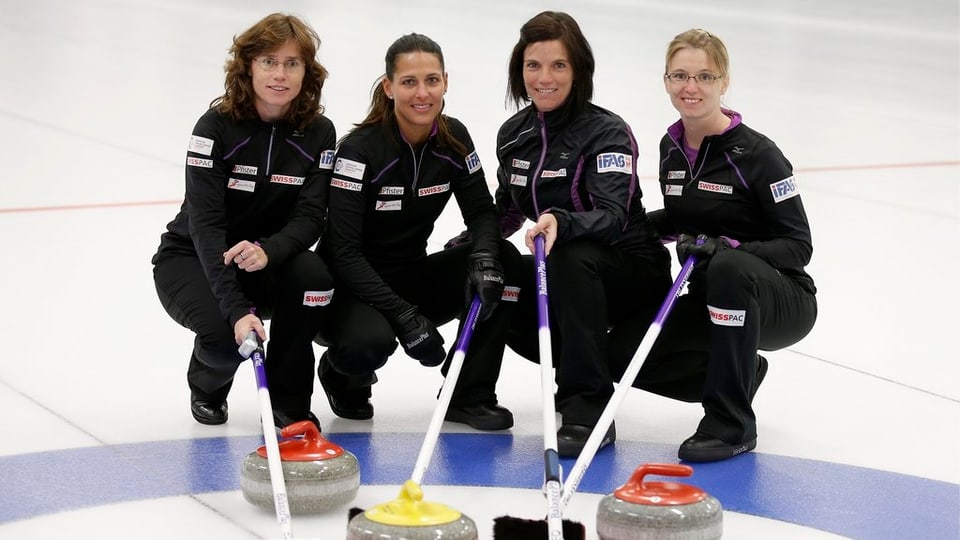 Das Curling-Team posiert mit Steinen und Besen auf dem Eis.