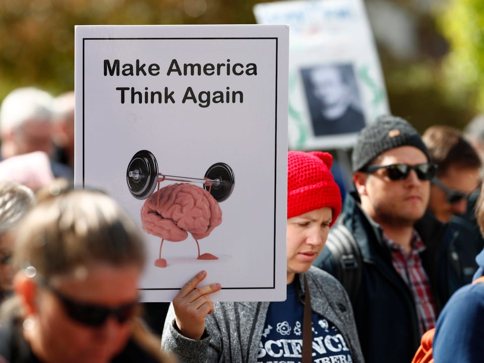 Eine Frau hält ein Plakat, auf dem steht: «Make America Think Again».