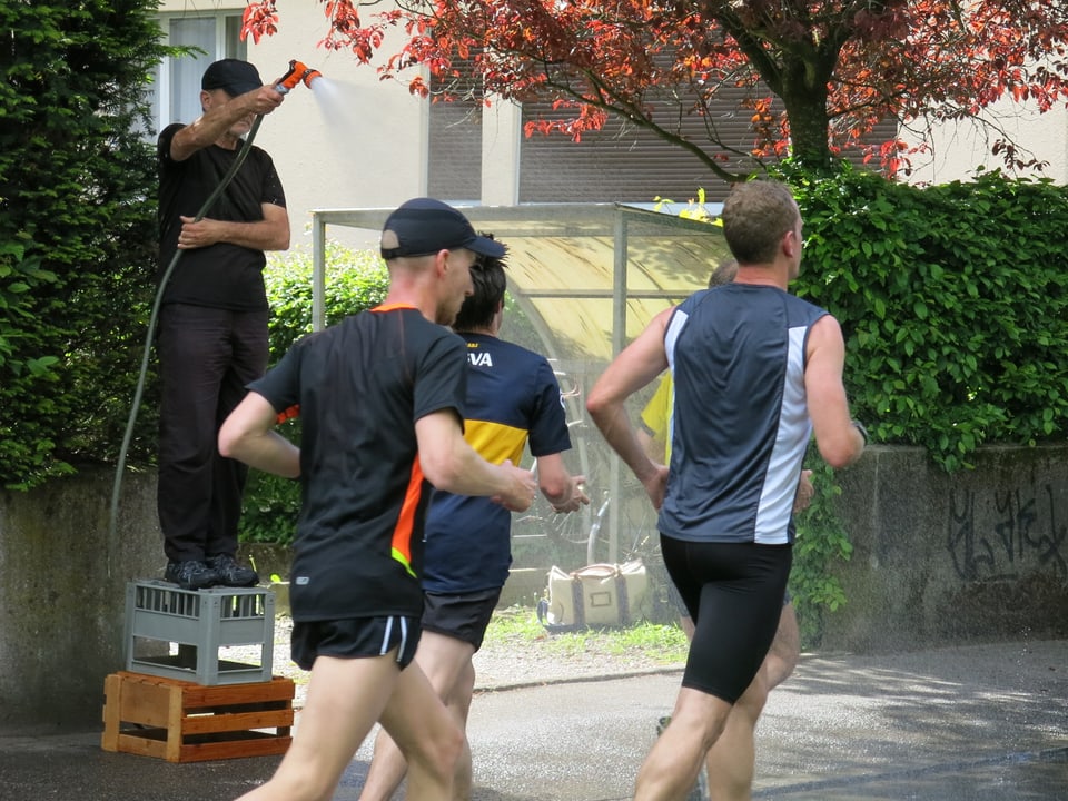 Ein Mann steht auf einer Kiste und duscht die Läufer mit einem Gartenschlauch.