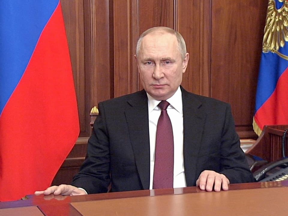Putin sitzt bei seiner Ansprache an die Nation an einem Schreibtisch. Im Hintergrund stehen Russland-Flaggen.
