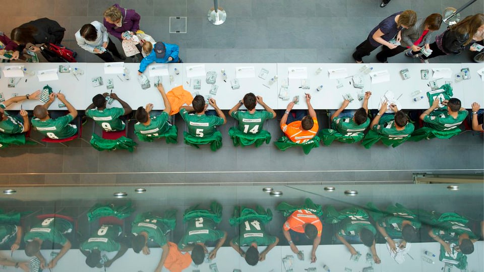 Blick von oben auf einen langen Tisch, an dem die Spieler des FC St. Gallen Autogramme verteilen.