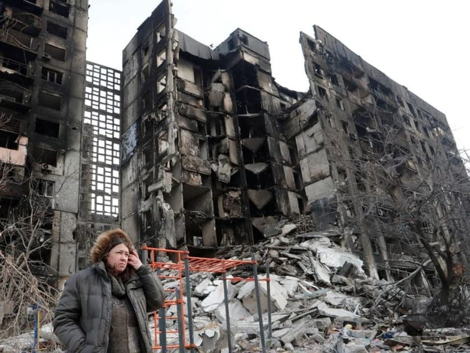Eine Frau steht vor einem zerstörten Gebäude.