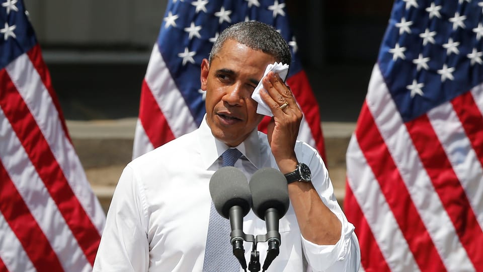 Barack Obama wischt sich den Schweiss mit einem weissen Taschentuch von der Stirn, vor ihm Mikrofone, hinter ihm US-Flaggen.