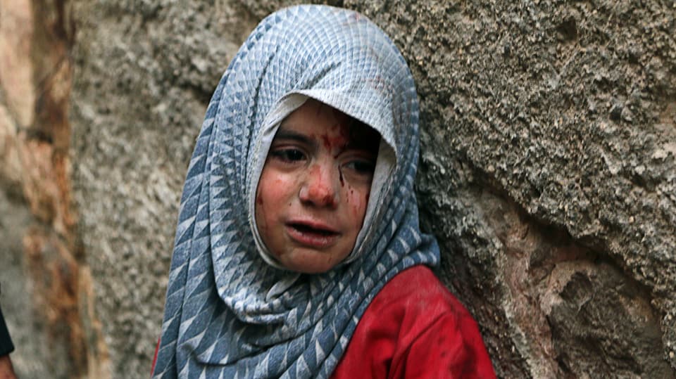 Kleines Mädchen mit Blutspuren im Gesicht drückt sich an eine Mauer.