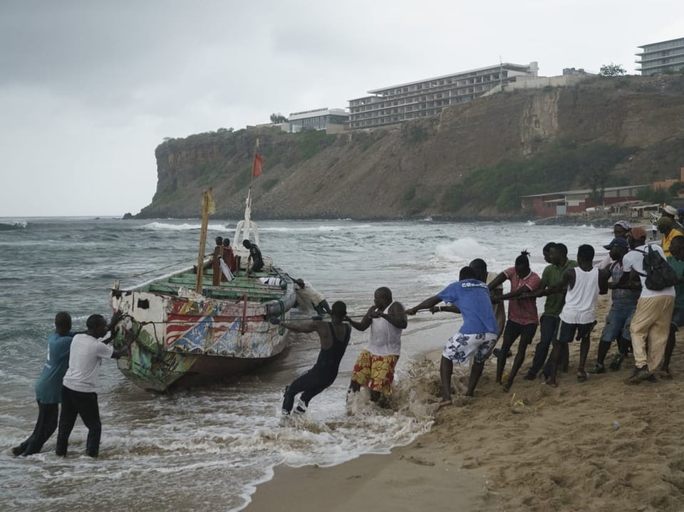 Menschen ziehen ein Holzboot an einem Seil vom Strand aus an Land