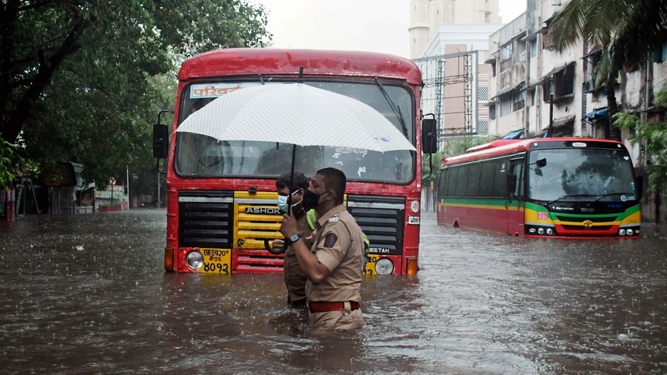 Ein indischer Polizit hilft einem Busfahrer die überschwemmte Starsse zu überqueren. 