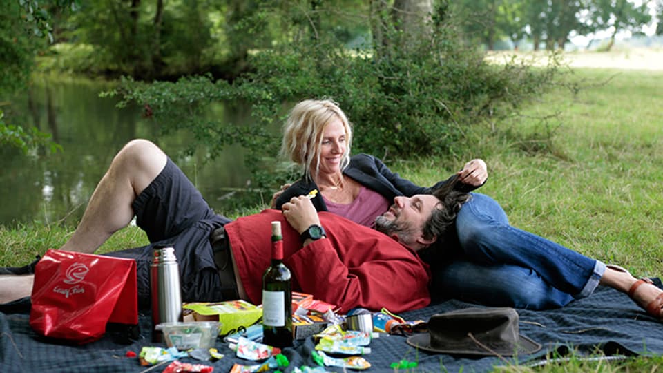 Der Protagonist und seine Frau geniessen ein Picknick am Rande des Flusses. 